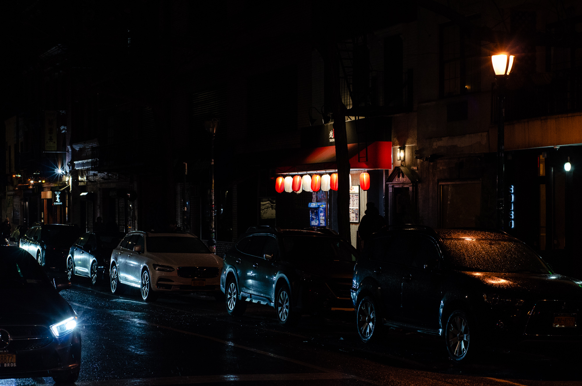 Cars parked along NYC at night with Japanese lanterns in background